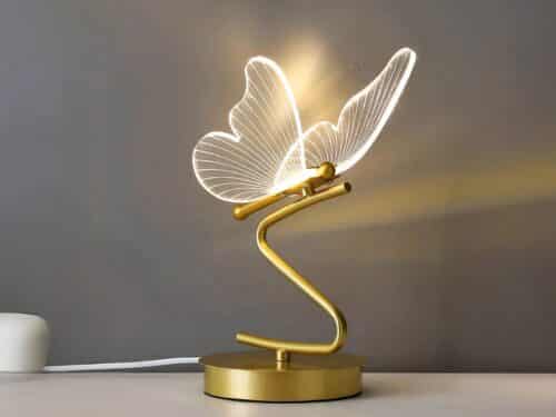 Lampe de chevet LED élégante en forme de papillon doré, sur une table.