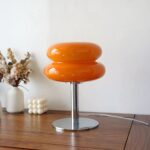 Lampe de chevet LED élégante et design en verre Lampe de chevet LED élégante et design en verre, de couleur orange en forme de macaron, sur une table.