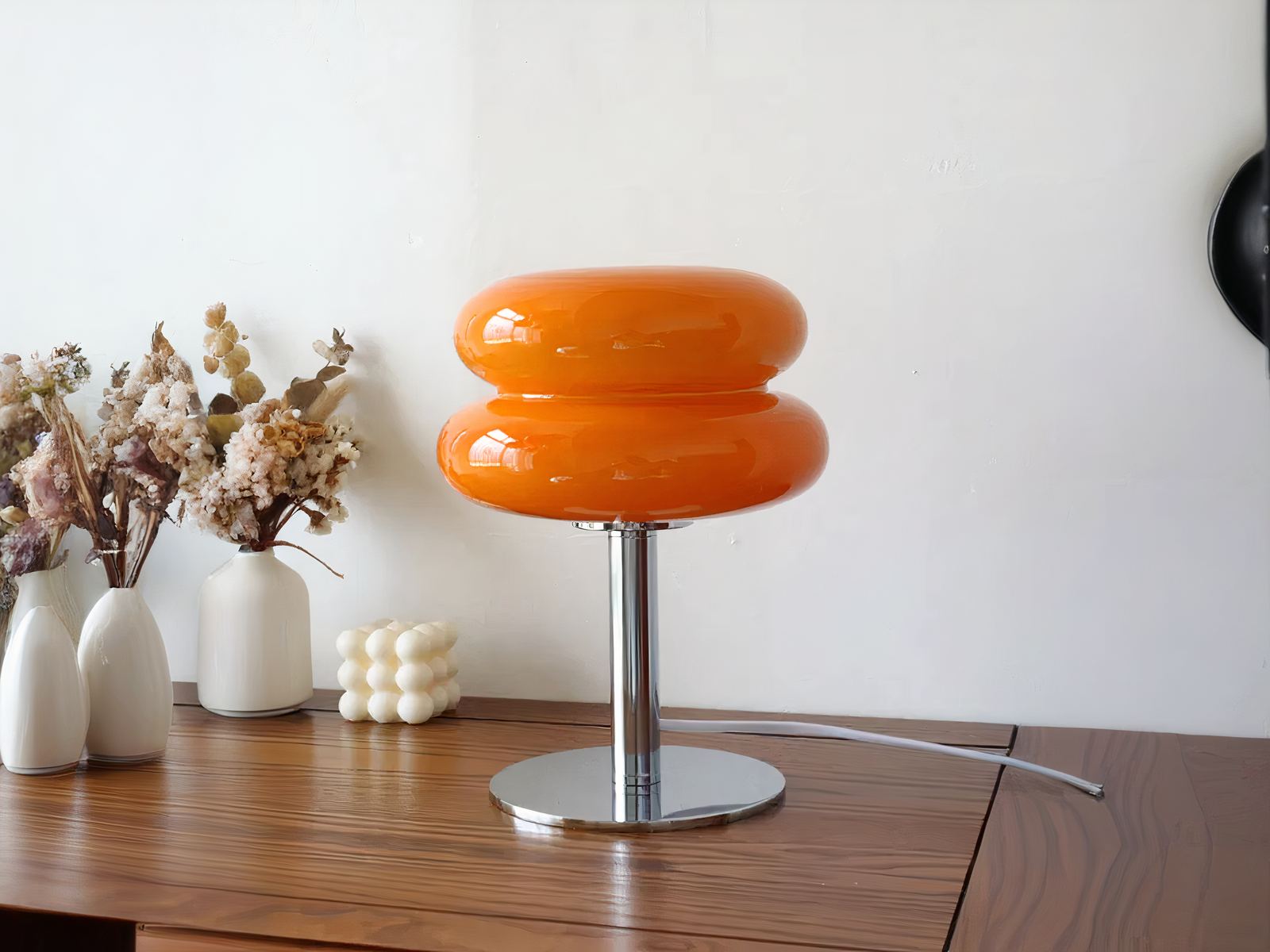 Lampe de chevet LED élégante et design en verre, de couleur orange en forme de macaron, sur une table.