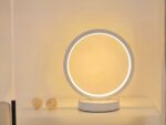 Lampe de chevet LED en forme d'anneau blanc, posée sur une table blanche.