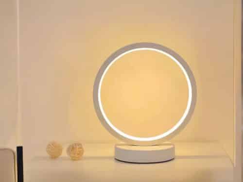 Lampe de chevet LED en forme d'anneau blanc, posée sur une table blanche.