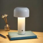 Lampe de chevet LED en forme de champignon, de couleur blanche, posée sur un livre sur une table.