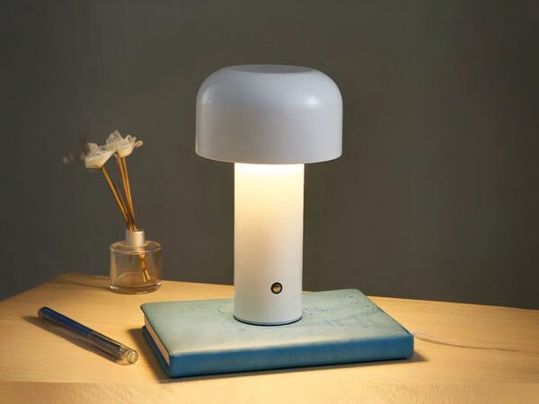 Lampe de chevet LED en forme de champignon, de couleur blanche, posée sur un livre sur une table.