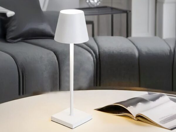 Lampe de chevet LED rechargeable et blanche avec abat jour, sur une table.