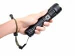 Lampe torche LED étanche et rechargeable tenue dans une main et sur fond blanc