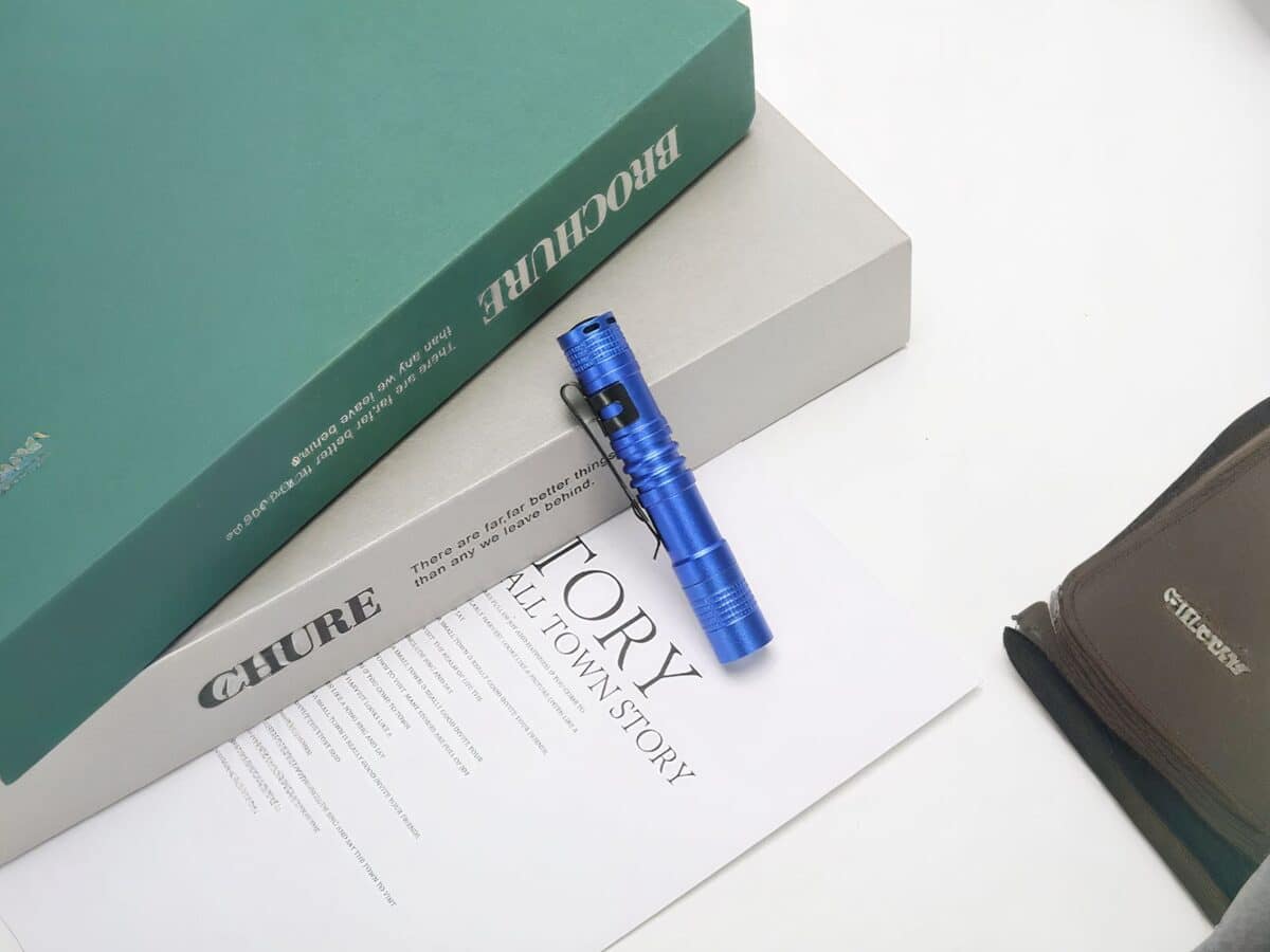 Lampe torche LED petit format avec clip intégré bleue sur une table contre des livres