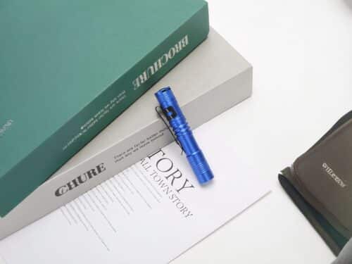 Lampe torche LED petit format avec clip intégré bleue sur une table contre des livres