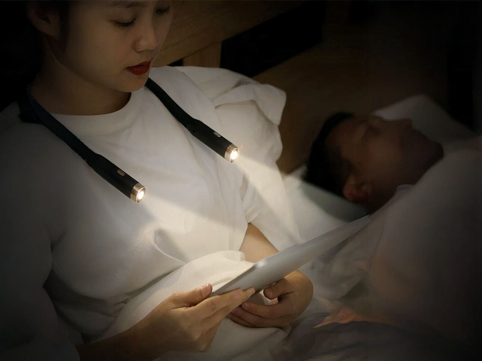 Femme dans son lit portant la liseuse Led de cou, allumée et lisant un livre dans le noir.