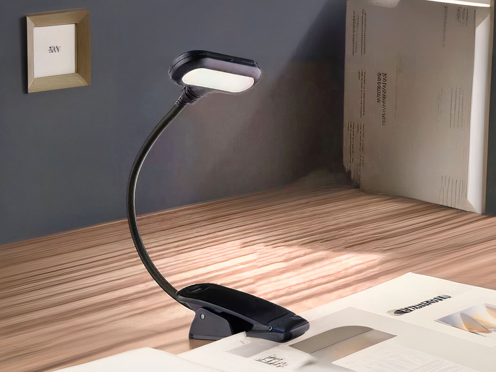 Liseuse LED noire flexible à pince Liseuse LED noire à pince avec tige flexible, allumée et accrochée à un livre. Le tout sur un bureau en bois.