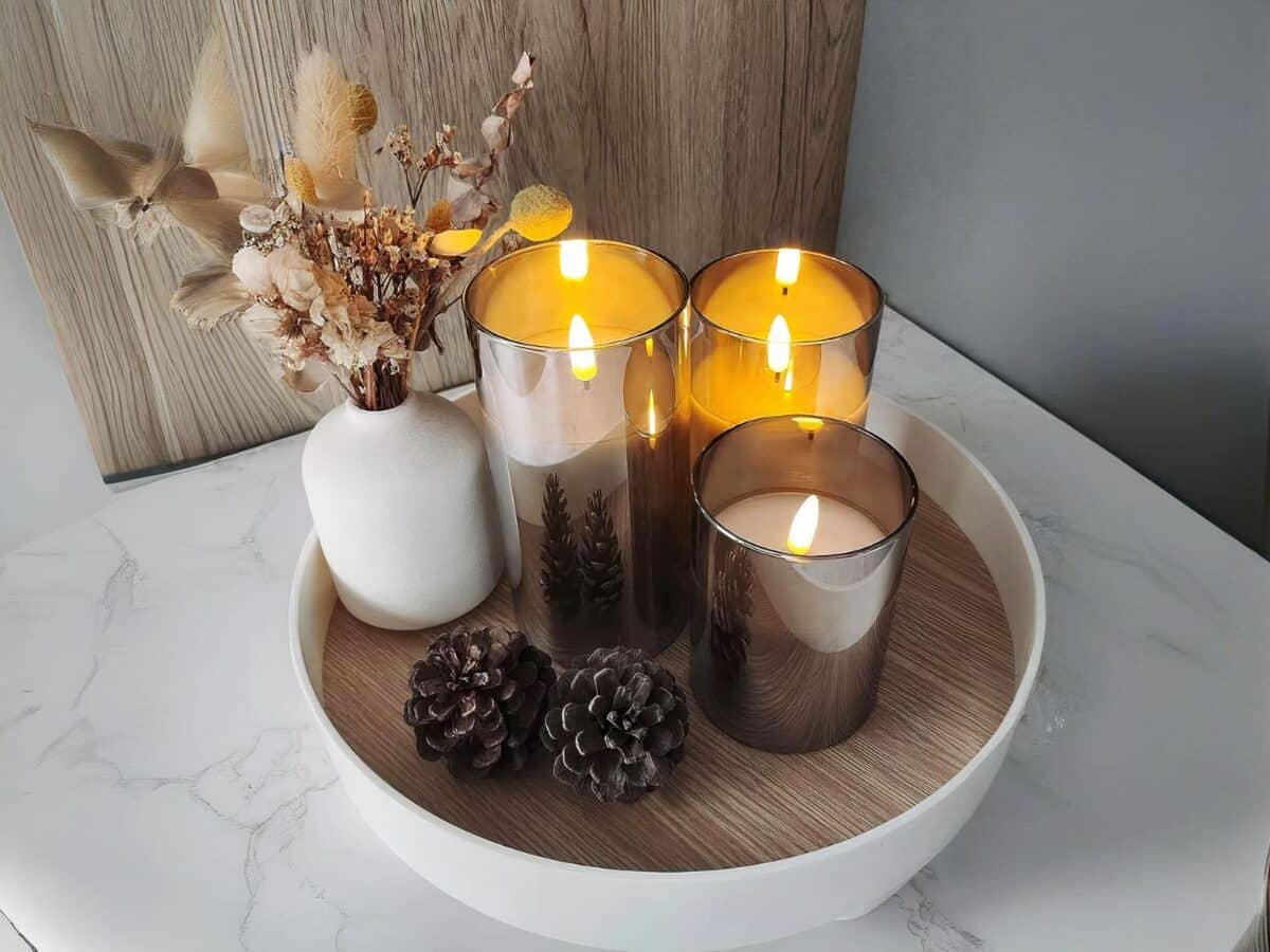 Lot 3 bougies LED à batterie avec télécommande Lot 3 bougies LED allumées et posées sur un plateau rond en bois.