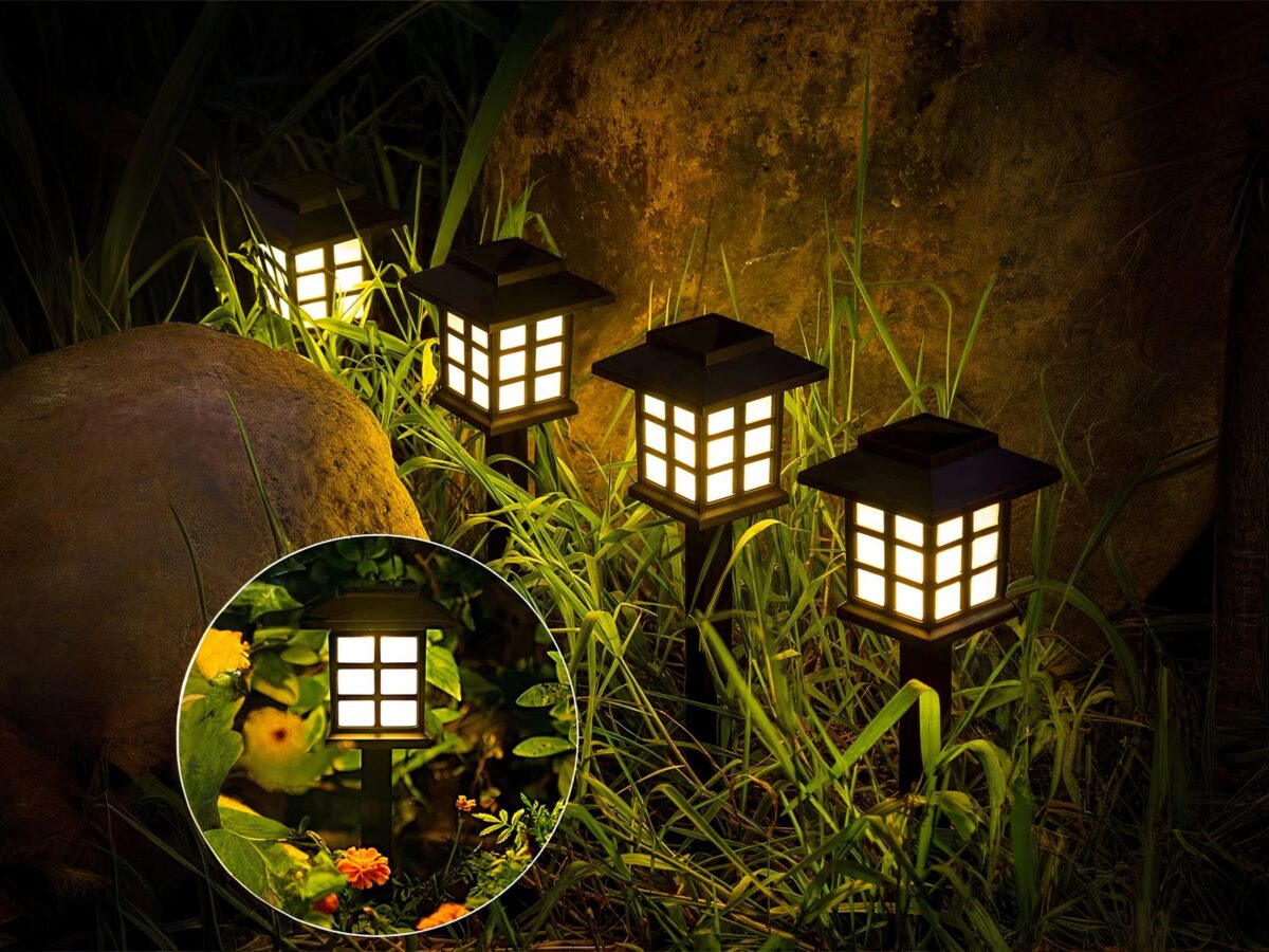 Lot de 4 lampes LED solaires noires style lanternes design, dans un massif.