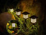 Lot de 4 lampes LED solaires noires style lanternes design, dans un massif.