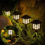 Lot de 4 lampes LED solaires noires style lanternes design Lot de 4 lampes LED solaires noires style lanternes design, dans un massif.