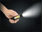 Mini lampe led multifonctionnelle étanche et noire, tenue dans une main, projetant une lumière blanche, sur un fond noir.