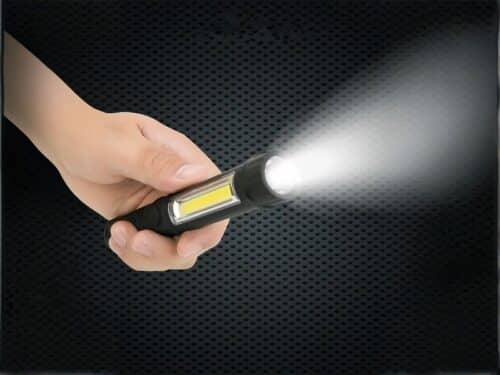 Mini lampe led multifonctionnelle étanche et noire, tenue dans une main, projetant une lumière blanche, sur un fond noir.