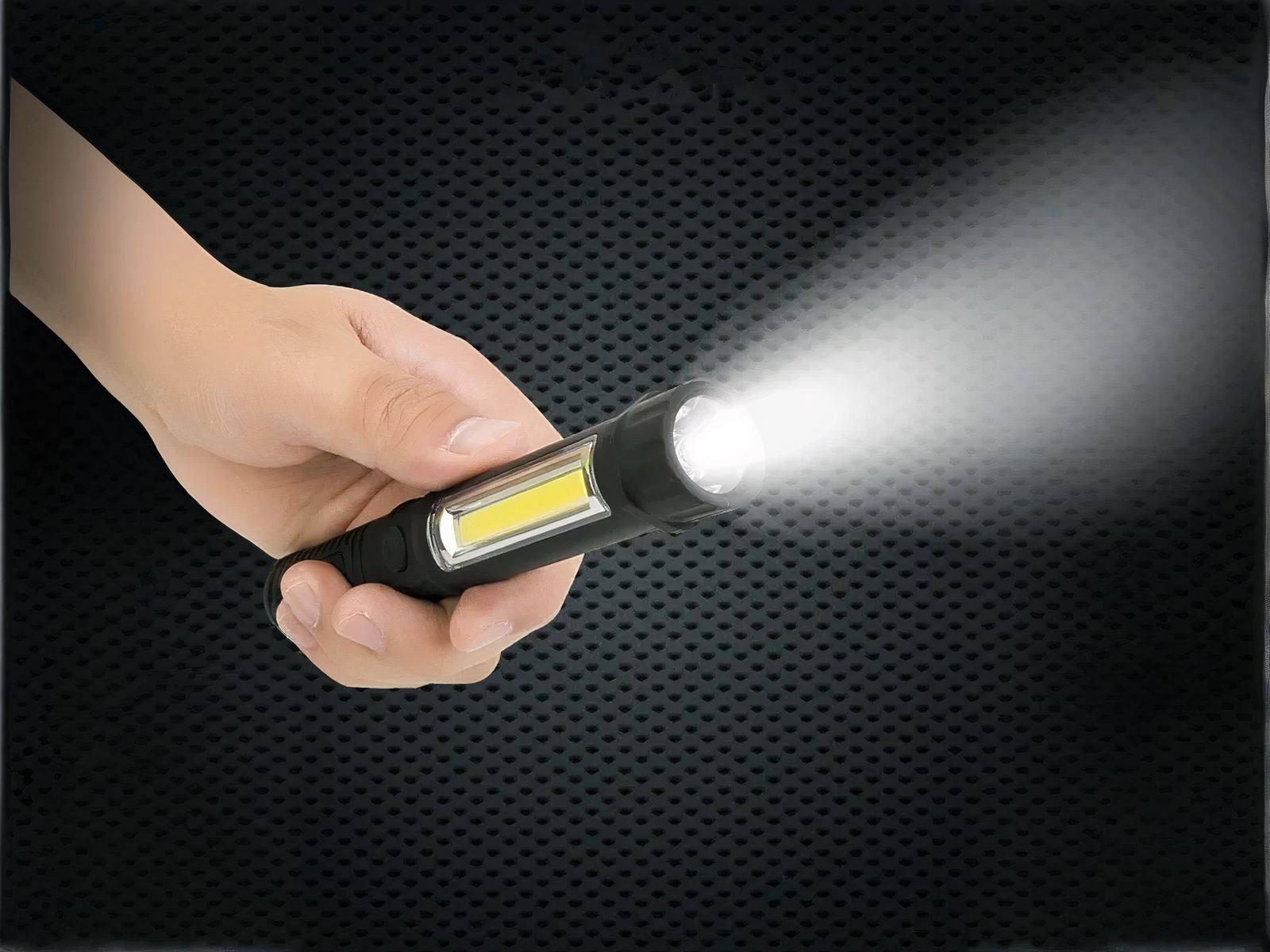 Mini lampe led multifonctionnelle étanche et noire Mini lampe led multifonctionnelle étanche et noire, tenue dans une main, projetant une lumière blanche, sur un fond noir.