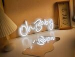 Néon LED Blanche avec inscription Oh Baby, sur une table posé contre un mur.