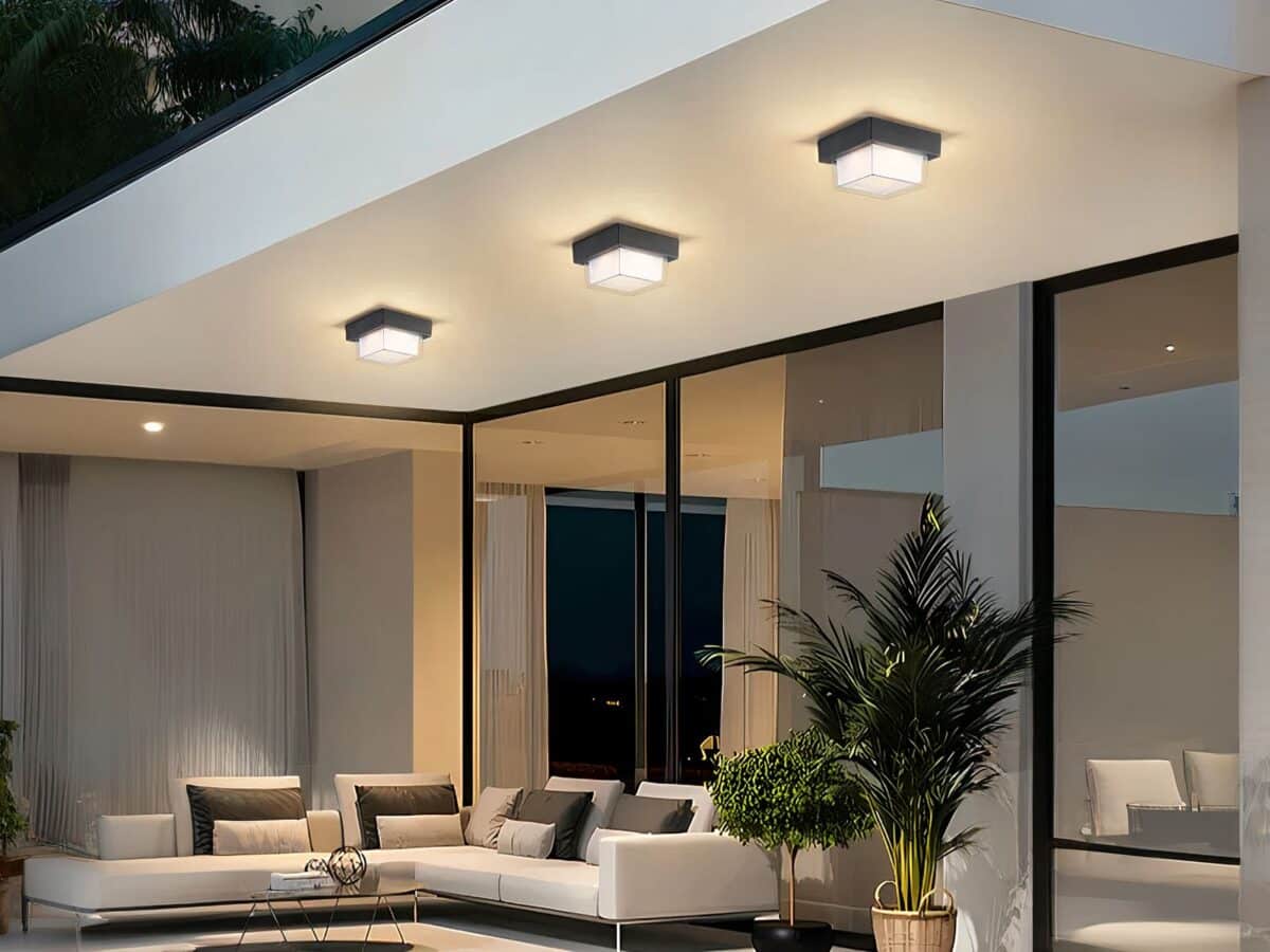 Plafonnier LED exterieur robuste et design Plafonnier LED exterieur robuste et design installé sur le plafond d'une terrasse avec un canapé, des baies vitrées et des plantes vertes en dessous