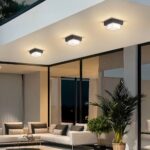 Plafonnier LED exterieur robuste et design installé sur le plafond d'une terrasse avec un canapé, des baies vitrées et des plantes vertes en dessous