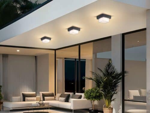 Plafonnier LED exterieur robuste et design installé sur le plafond d'une terrasse avec un canapé, des baies vitrées et des plantes vertes en dessous