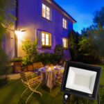 Projecteur extérieur LED avec détecteur de mouvement Projecteur extérieur LED avec détecteur de mouvement installé sur la façade d'une maison avec une table et des chaises dans un jardin