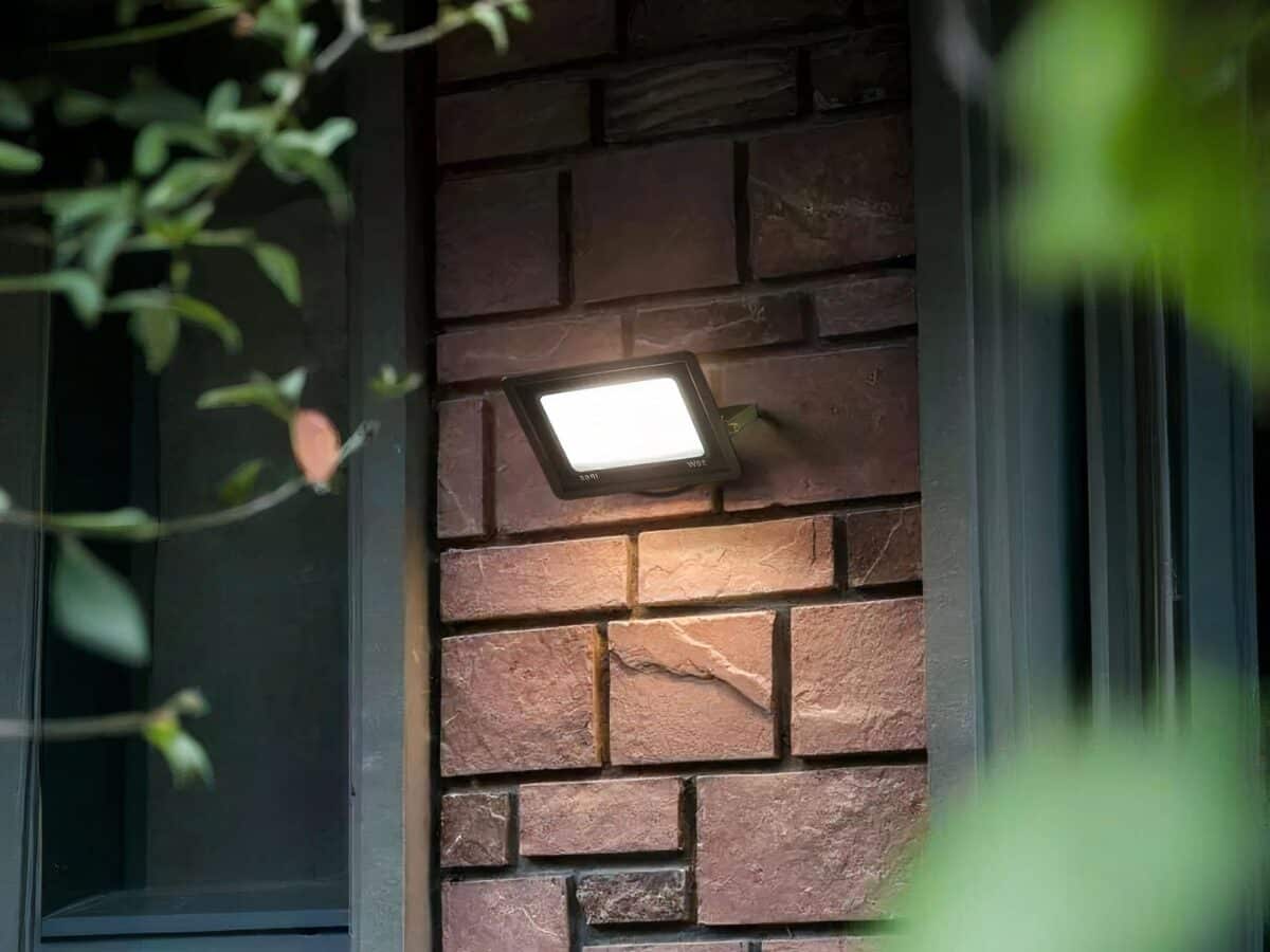 Projecteur extérieur LED étanche et durable installé sur la façade d'une maison avec des plantes vertes à droite et à gauche