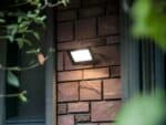 Projecteur extérieur LED étanche et durable installé sur la façade d'une maison avec des plantes vertes à droite et à gauche