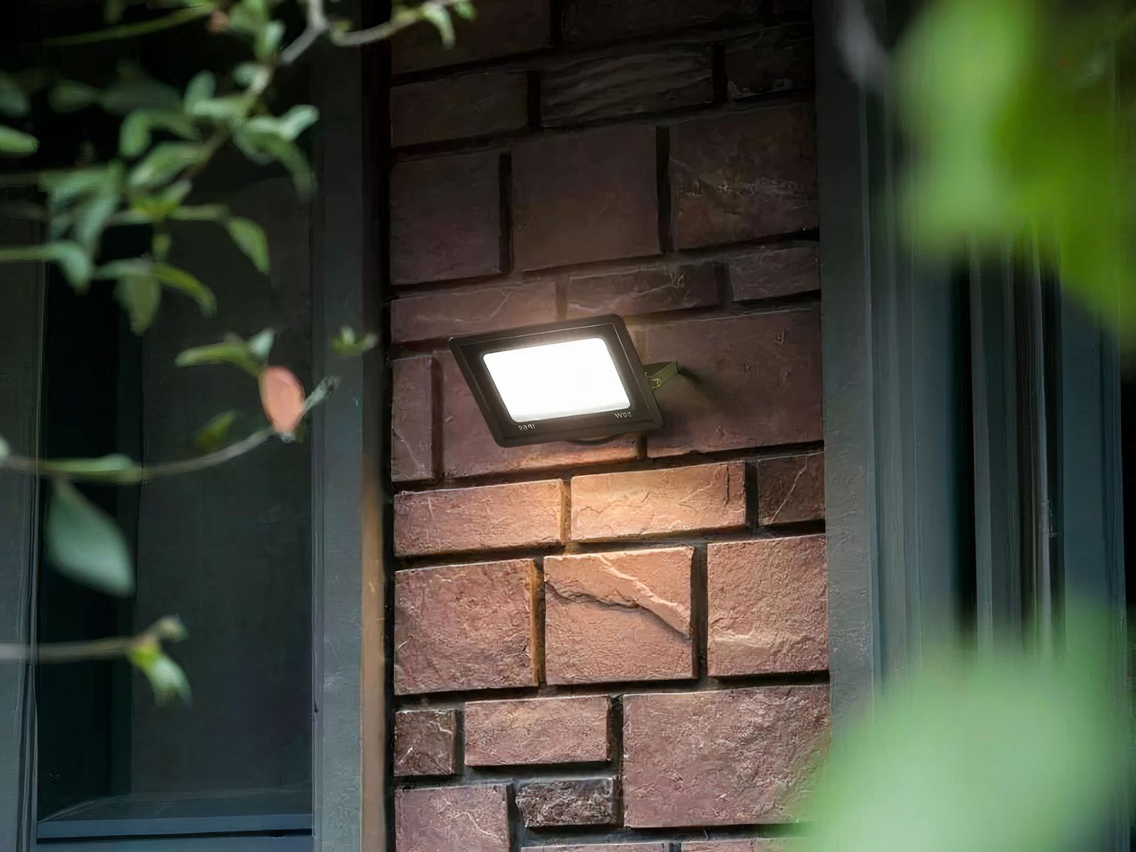 Projecteur extérieur LED étanche et durable installé sur la façade d'une maison avec des plantes vertes à droite et à gauche