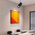 Projecteur LED design et rotatif installé sur un plafond avec un tableau contre le mur et une table en dessous