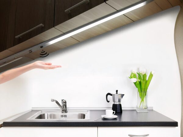 Réglette LED de cuisine avec capteur de balayage, allumée et installée sous un meuble haut au-dessus d'un évier.