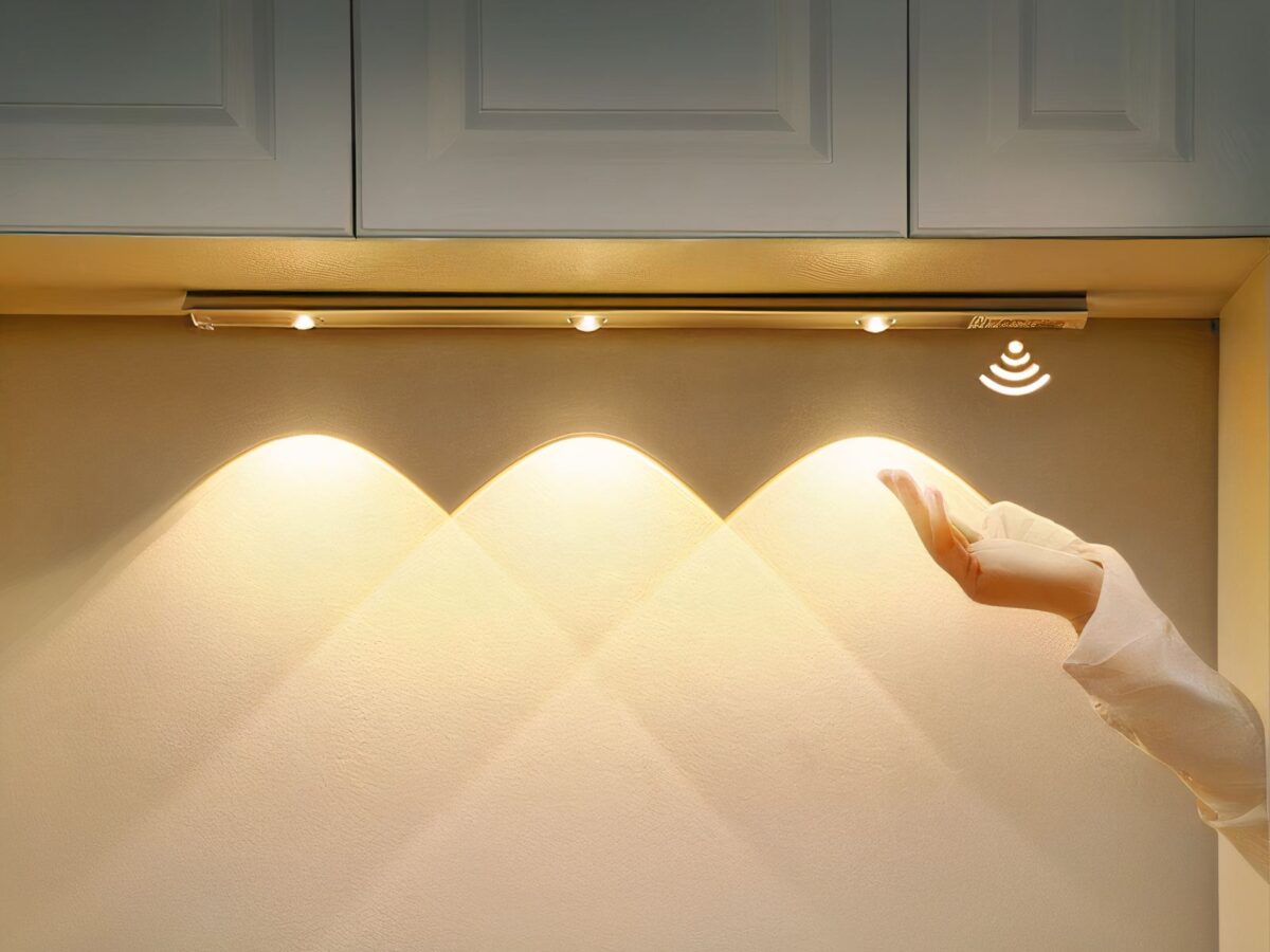 Réglette led cuisine rechargeable avec détecteur de mouvement Réglette LED de cuisine, allumée et installée sous un meuble haut de cuisine. Une main passe pour déclencher le détecteur de mouvement.