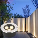 Spot LED extérieur encastrable imperméable et compact Spot LED extérieur encastrable imperméable et compact avec 3 sources lumineuses, en bas à gauche d'une photo de mur de jardin éclairé par le spot.