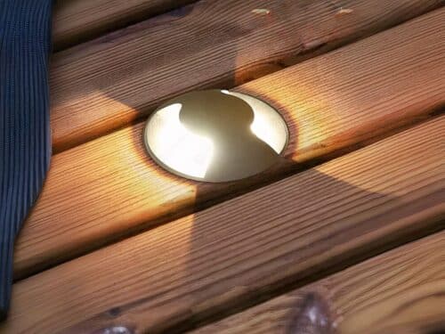Spot LED extérieur encastrable dans le sol en acier inoxydable, allumé et installé dans une lame de terrasse en bois.