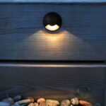 Spot LED extérieur noir et arrondi allumé et installé contre un mur en bois.