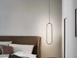 Suspension LED minimaliste ovale noire allumée, à côté d'un lit comme une lampe de chevet.
