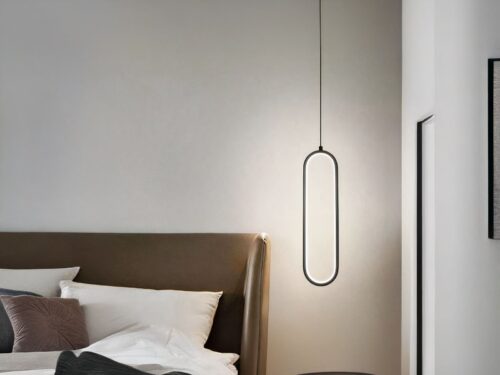 Suspension LED minimaliste ovale noire allumée, à côté d'un lit comme une lampe de chevet.