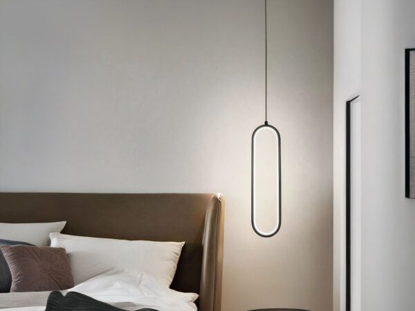 Suspension LED minimaliste ovale noire allumée, à côté d'un lit comme une lampe de chevet.