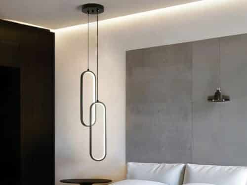 Suspension LED double ovale noire, installée à côté d'un lit comme une lampe de chevet.