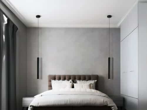 Chambre avec un grand lit et une tête de lit capitonnée marron, et une suspension LED tube noire de chaque côté du lit en guise de lampe de chevet.