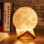 Veilleuse LED décorative en forme de lune Veilleuse LED décorative en forme de lune allumée sur un bureau avec des livres à côté