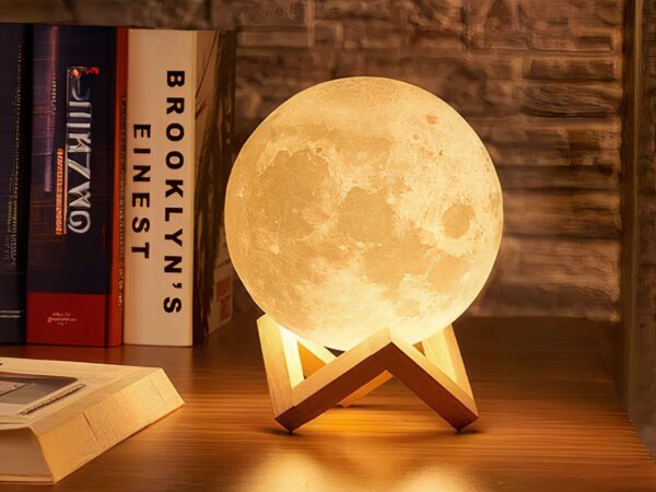 Veilleuse LED décorative en forme de lune allumée sur un bureau avec des livres à côté