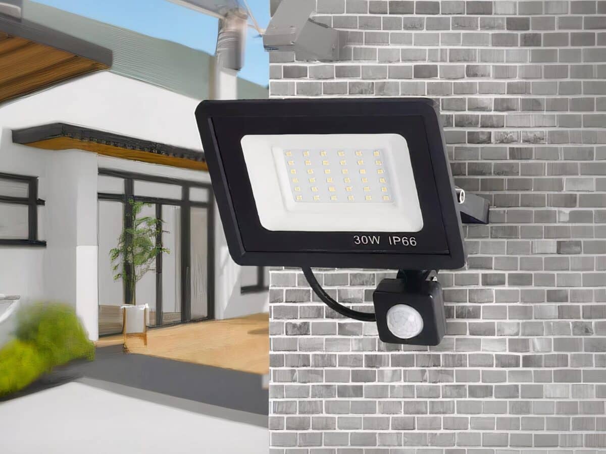 Projecteur LED extérieur à détecteur de mouvement installé sur un mur en briques grises.
