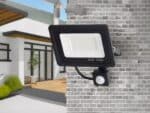 Projecteur LED extérieur à détecteur de mouvement installé sur un mur en briques grises.