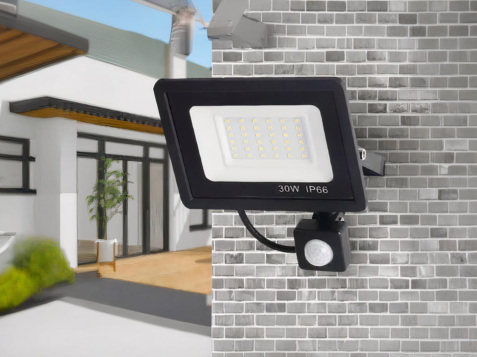 Projecteur LED extérieur à détecteur de mouvement installé sur un mur en briques grises.