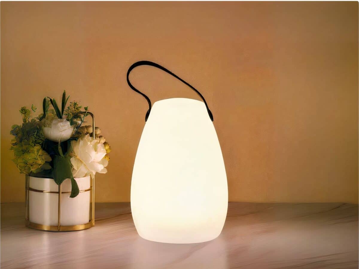 Lampe LED rechargeable télécommandée style lanterne posée sur une table avec un bouquet de fleurs