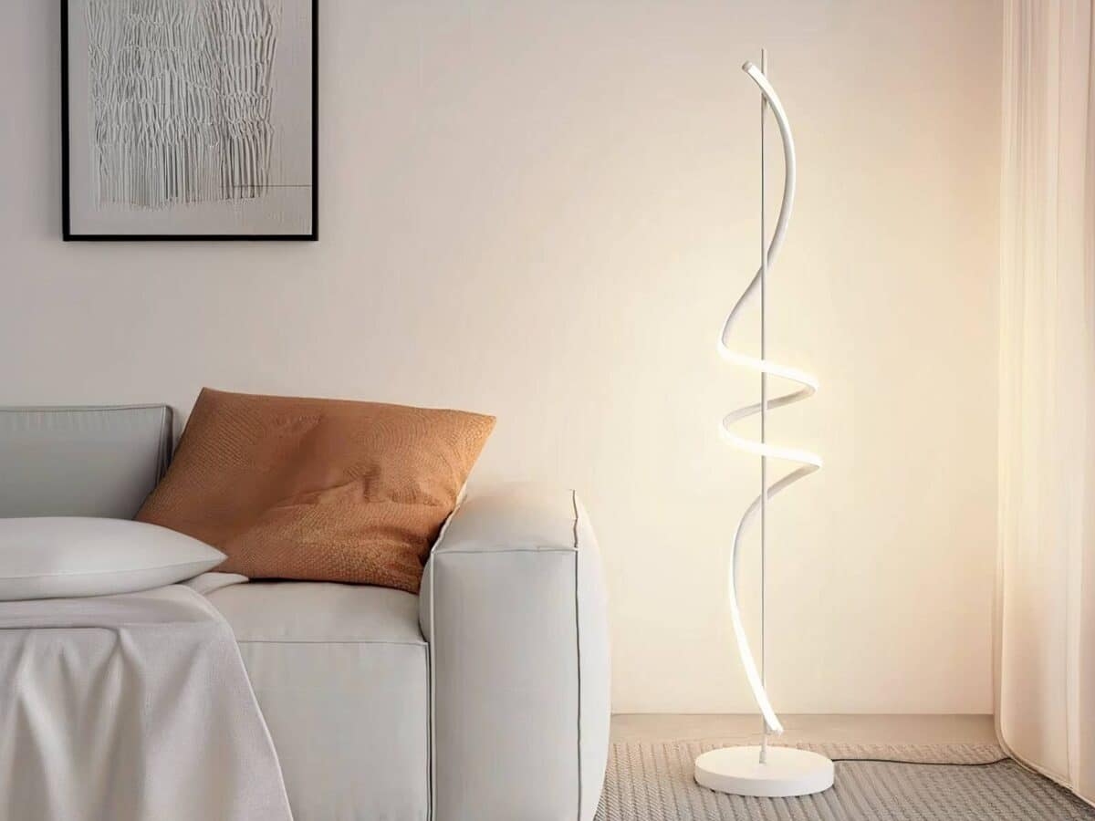 Lampadaire LED créatif spirale Lampadaire LED fer créatif spirale blanc allumé et installé à côté d'un canapé beige avec un coussin marron.