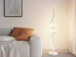 Lampadaire LED fer créatif spirale blanc allumé et installé à côté d'un canapé beige avec un coussin marron.