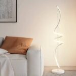 Lampadaire LED fer créatif spirale blanc allumé et installé à côté d'un canapé beige avec un coussin marron.