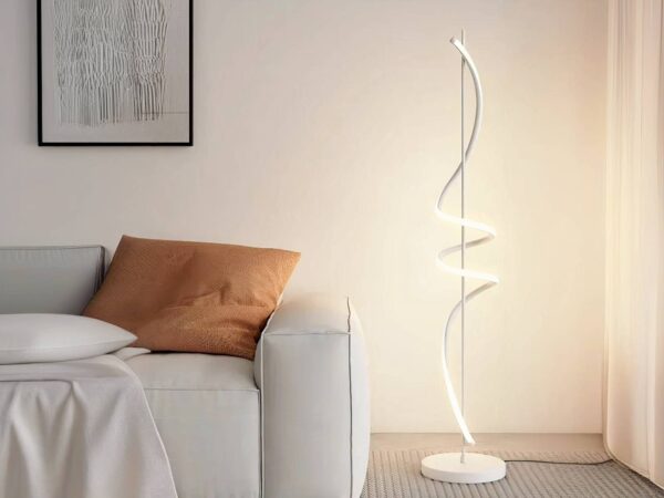 Lampadaire LED fer créatif spirale blanc allumé et installé à côté d'un canapé beige avec un coussin marron.