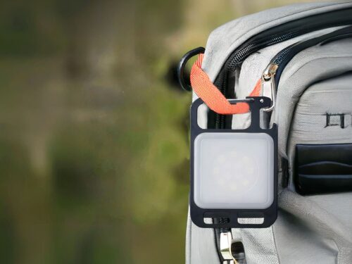 Lampe de travail LED mini porte-clés, accrochée à un sac à dos gris.